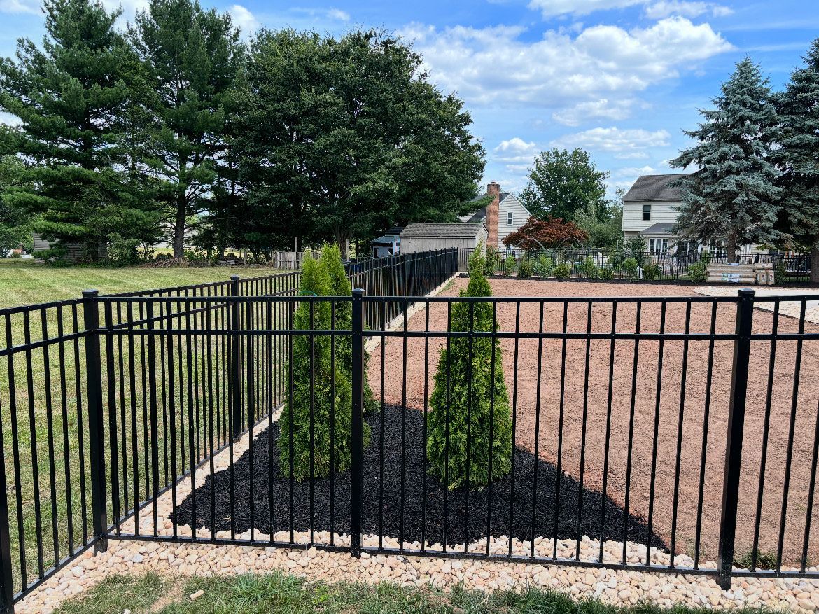 A black fence surrounds a yard with trees and gravel.