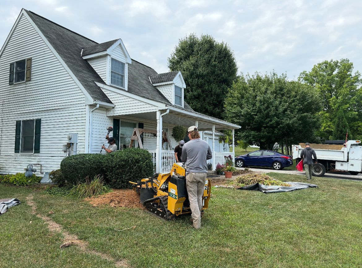 A man is standing in front of a house with a stump grinder.