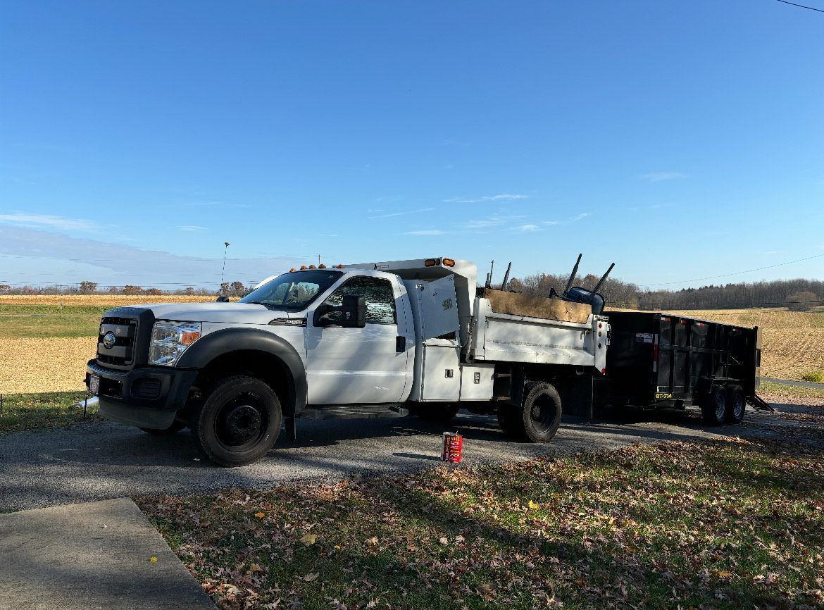A white dump truck is parked on the side of the road next to a field.