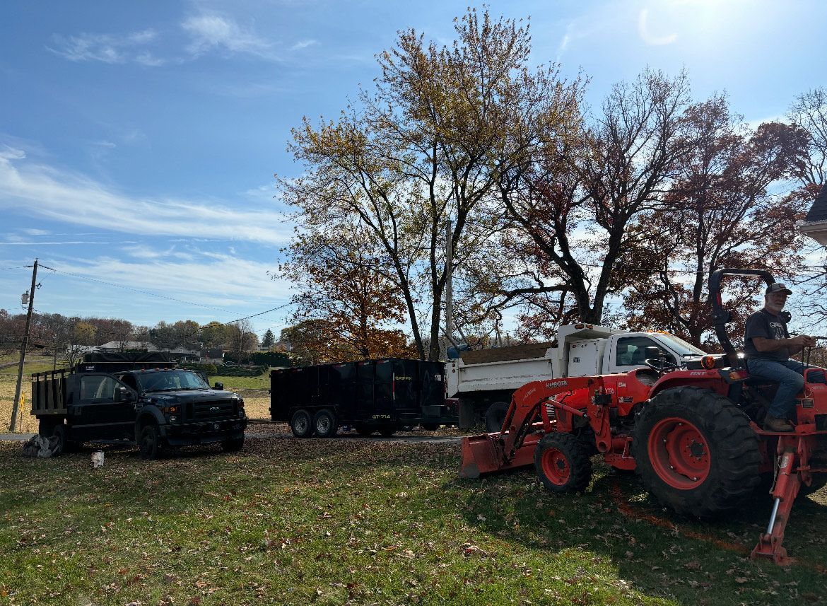 A man is riding a tractor in a field next to a truck.