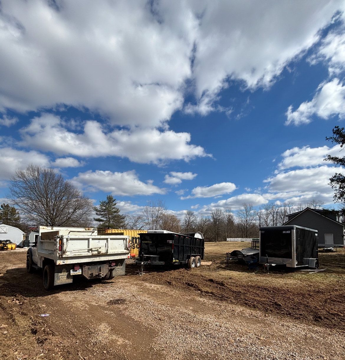 A dump truck and a trailer are parked in a dirt field.