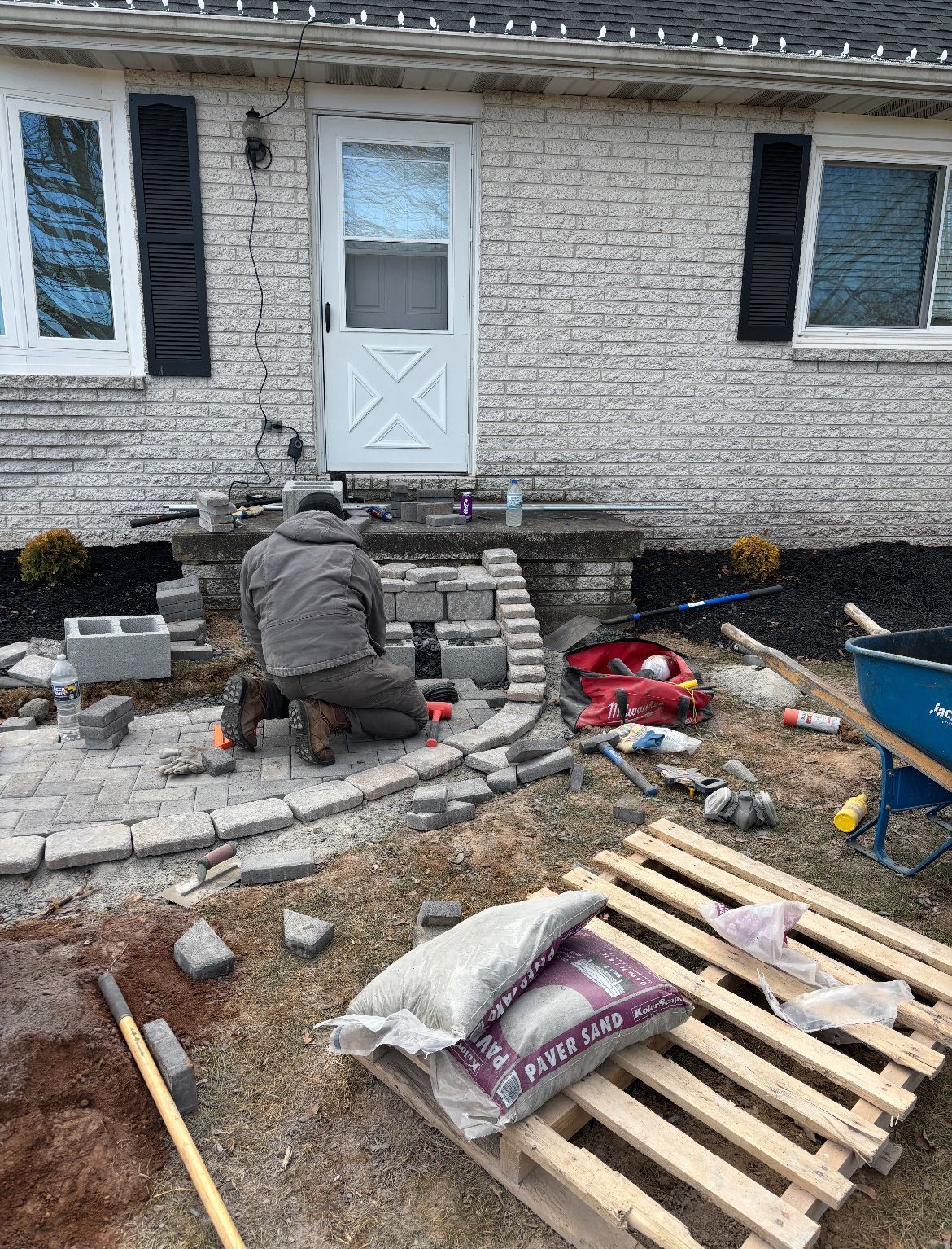 A man is kneeling down in front of a brick house.