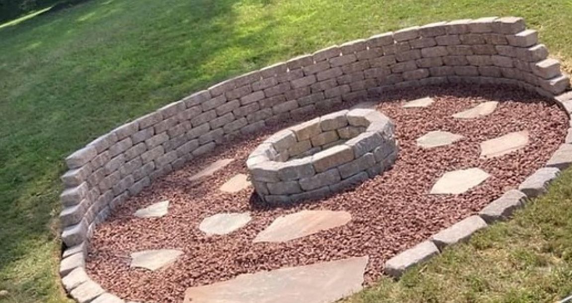 A fire pit is surrounded by a stone wall and gravel.