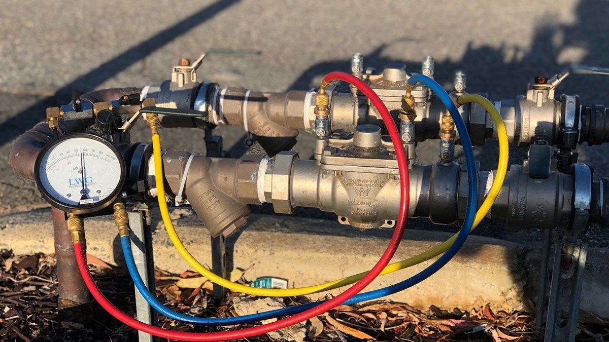 A water pressure gauge and backflow preventer with connecting hoses.