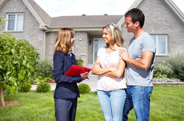 Real estate agent showing a house to a smiling couple in front of a suburban home