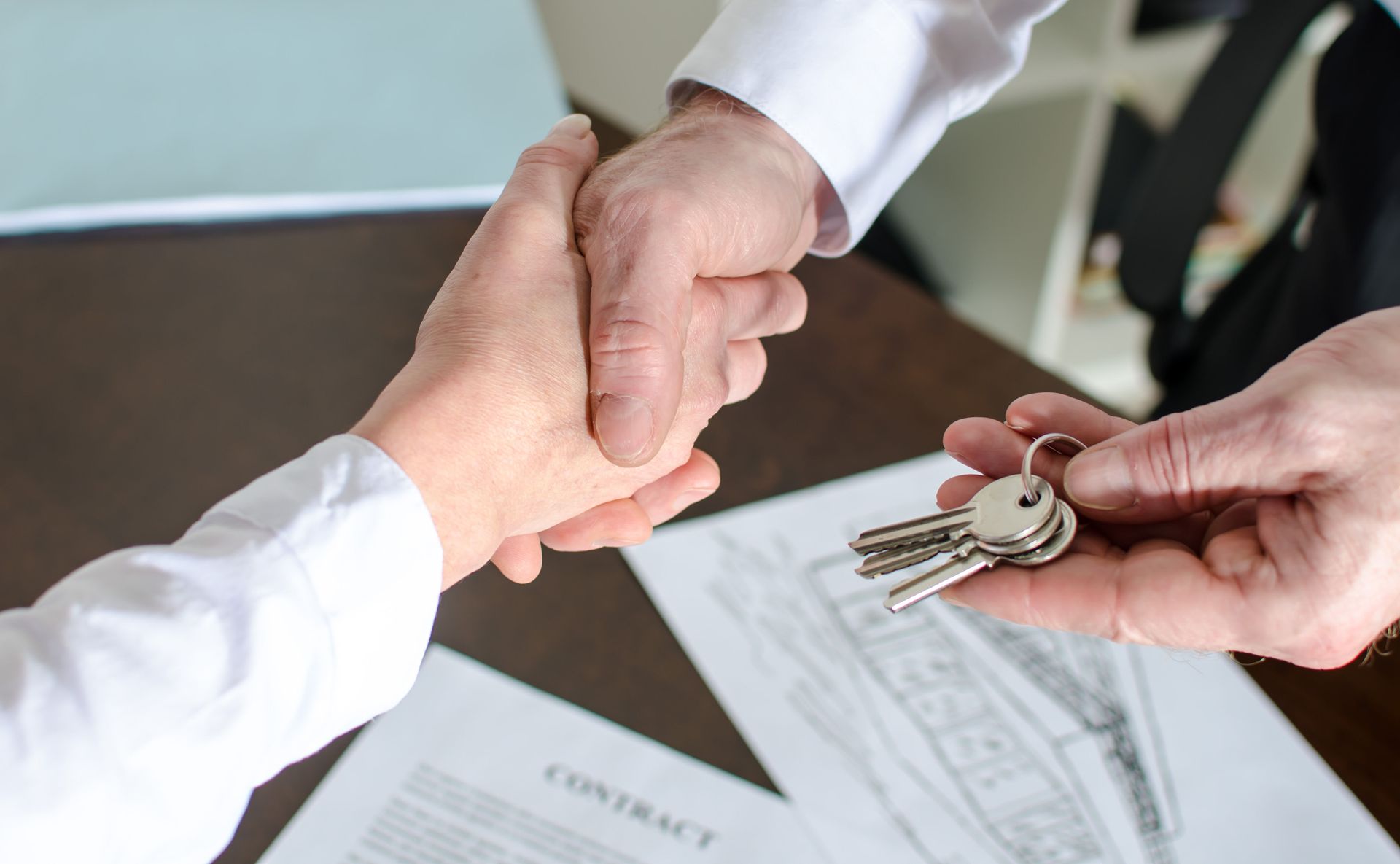 Hands exchanging house keys over a contract on a desk during a real estate transaction