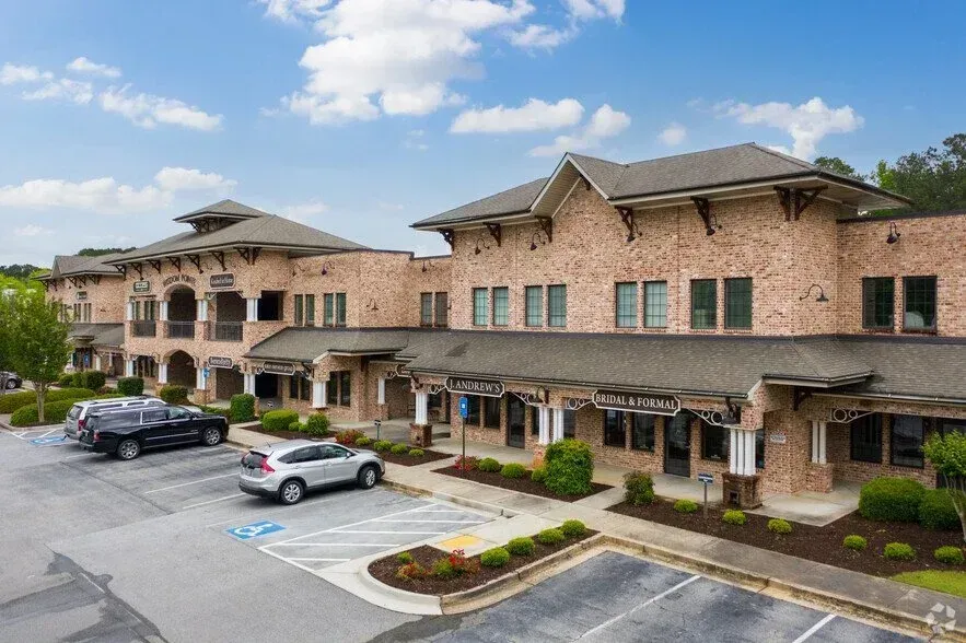 Brick office building with storefronts and parked cars in a small parking lot