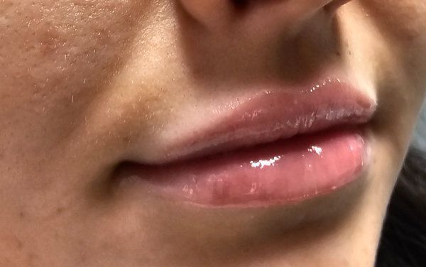 A close-up view of shiny, plump, pink-toned lips with a clear gloss finish.