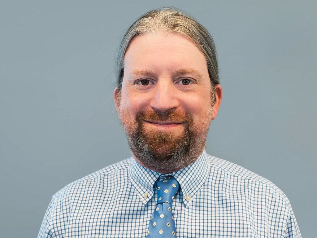 A man with a beard is wearing a plaid shirt and tie.