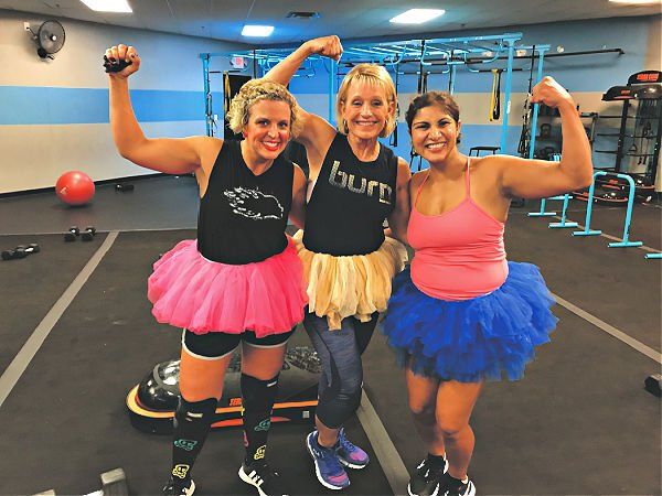 Three women in tutus are posing for a picture in a gym