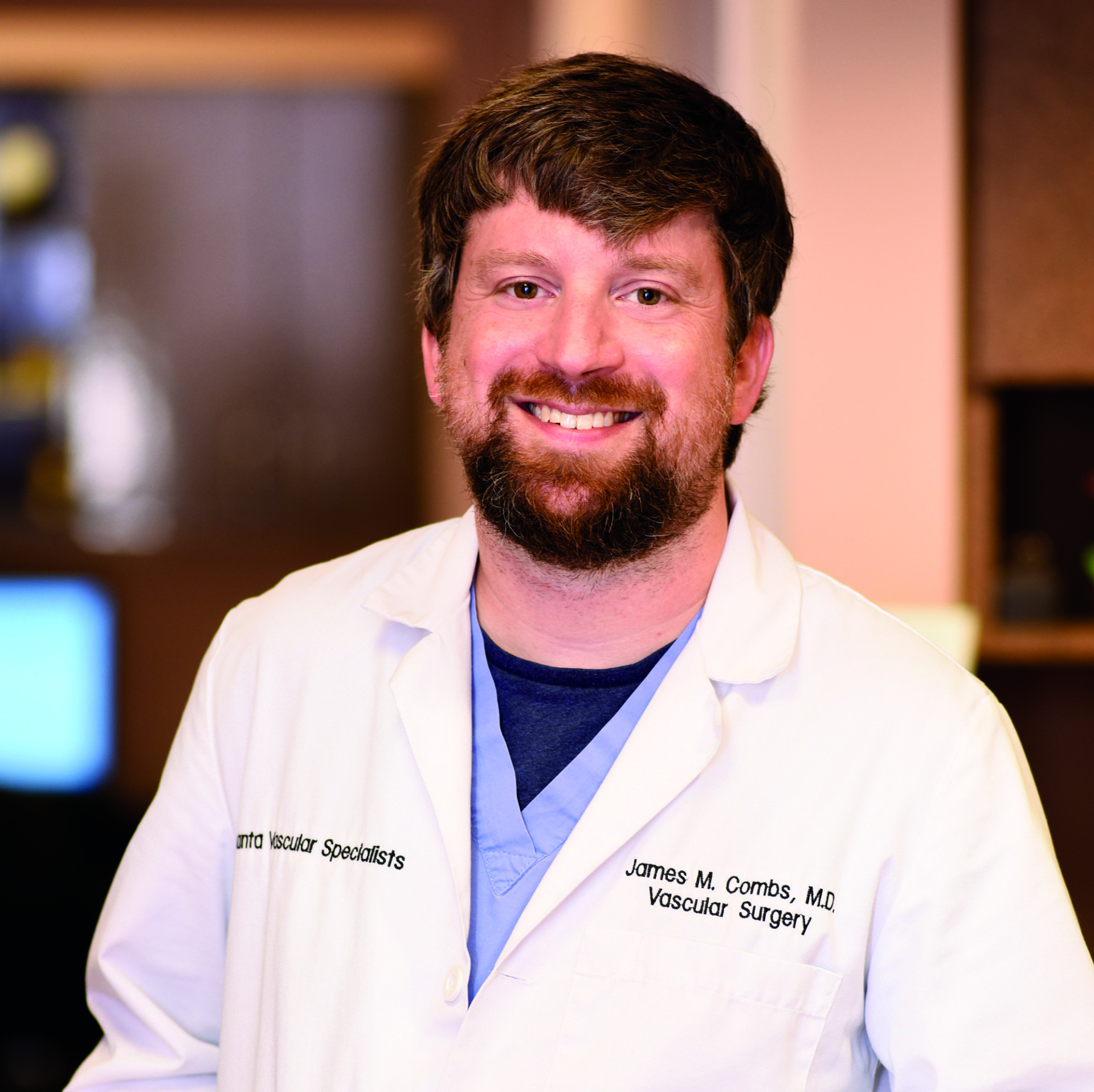 A man with a beard is wearing a white lab coat and smiling