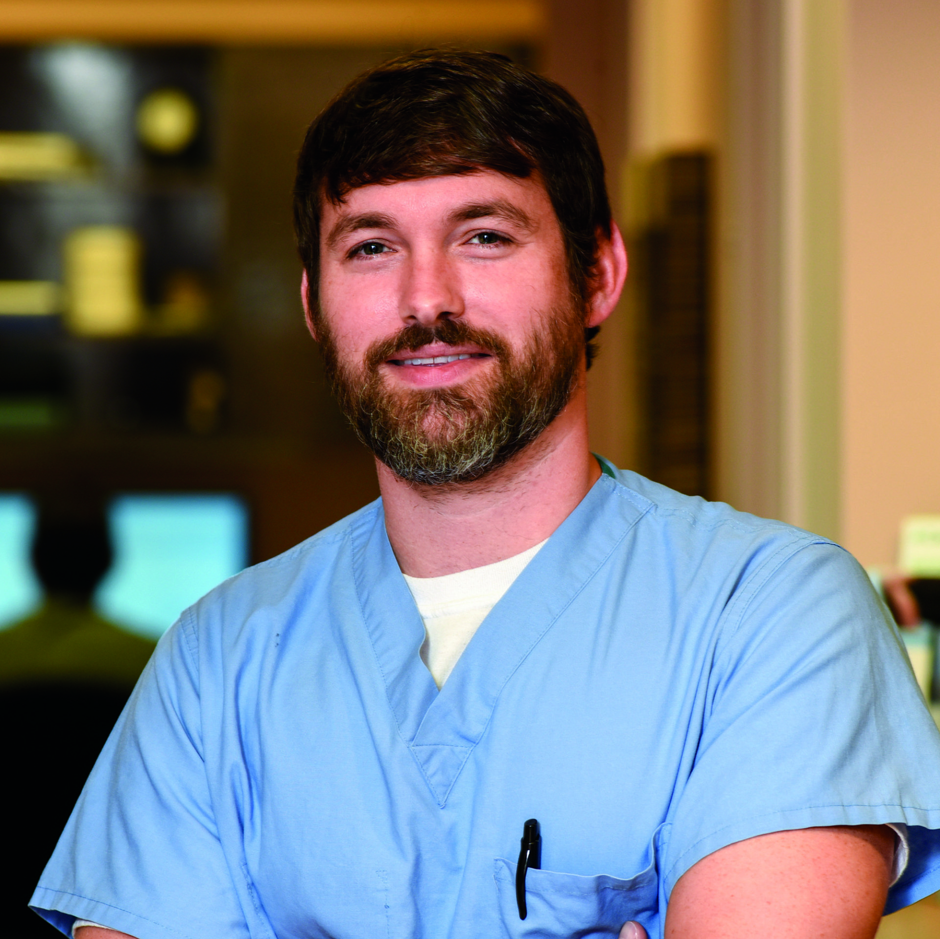 A man with a beard is wearing a blue scrub top