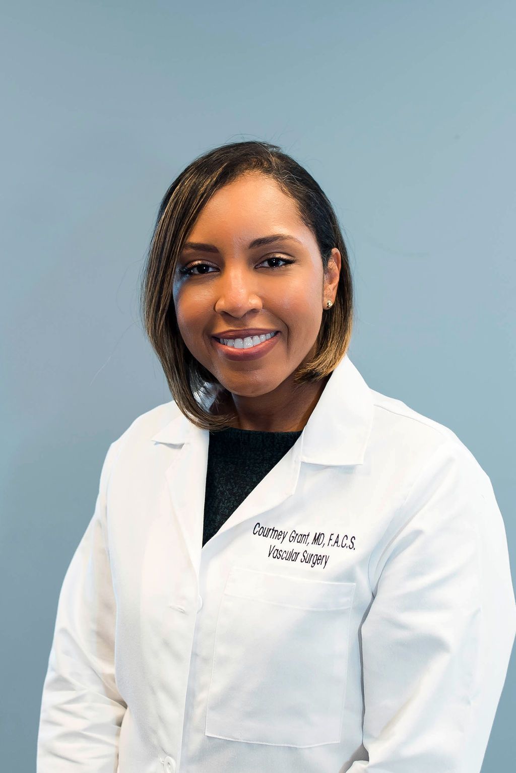 A woman in a white lab coat is smiling for the camera.