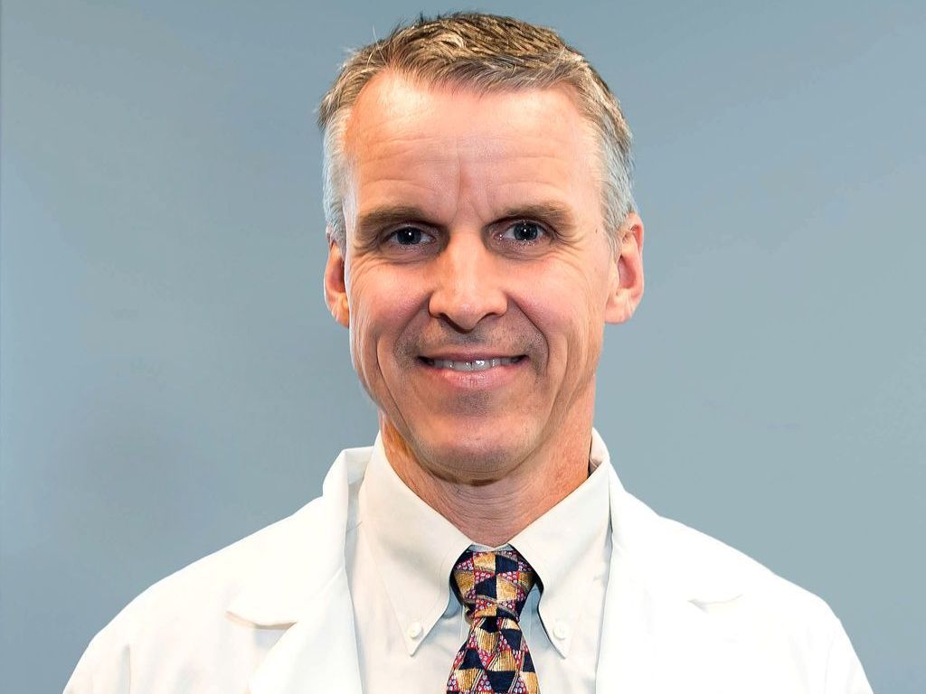 A man in a white coat and tie is smiling for the camera.