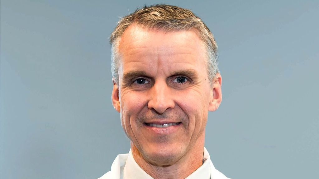 A man in a white coat and tie is smiling for the camera.