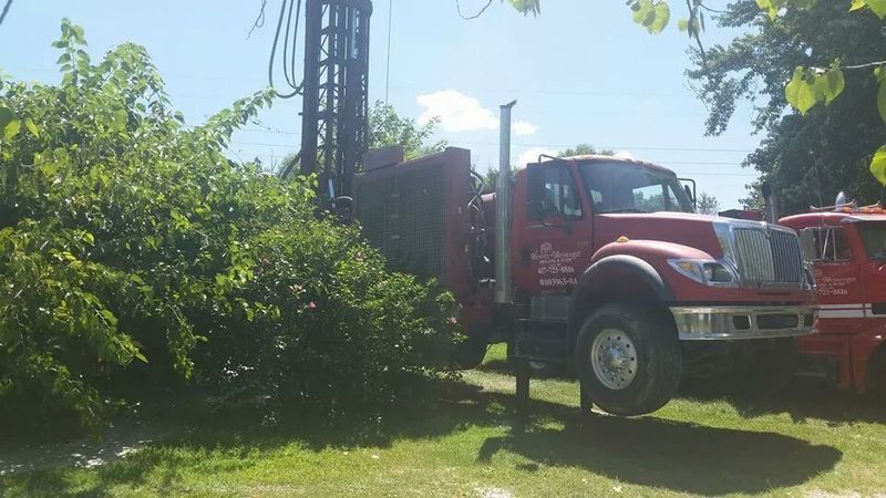 A red truck is parked in a grassy field next to a tree.