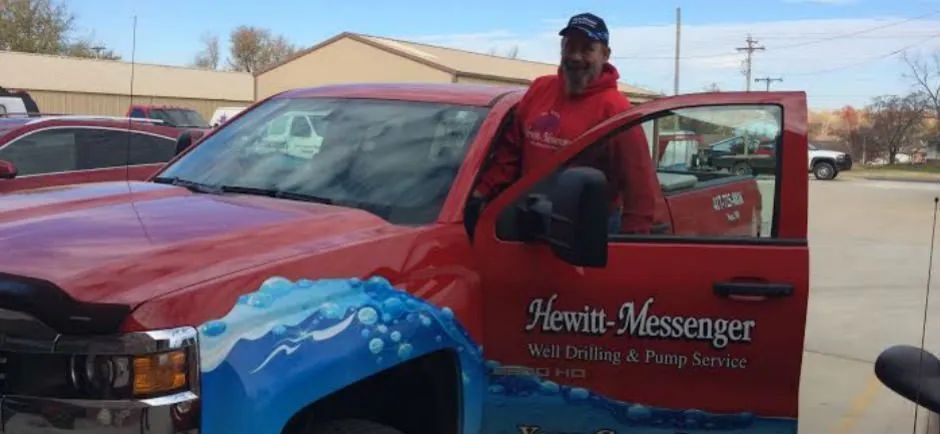 A man is standing next to a red truck with the door open.