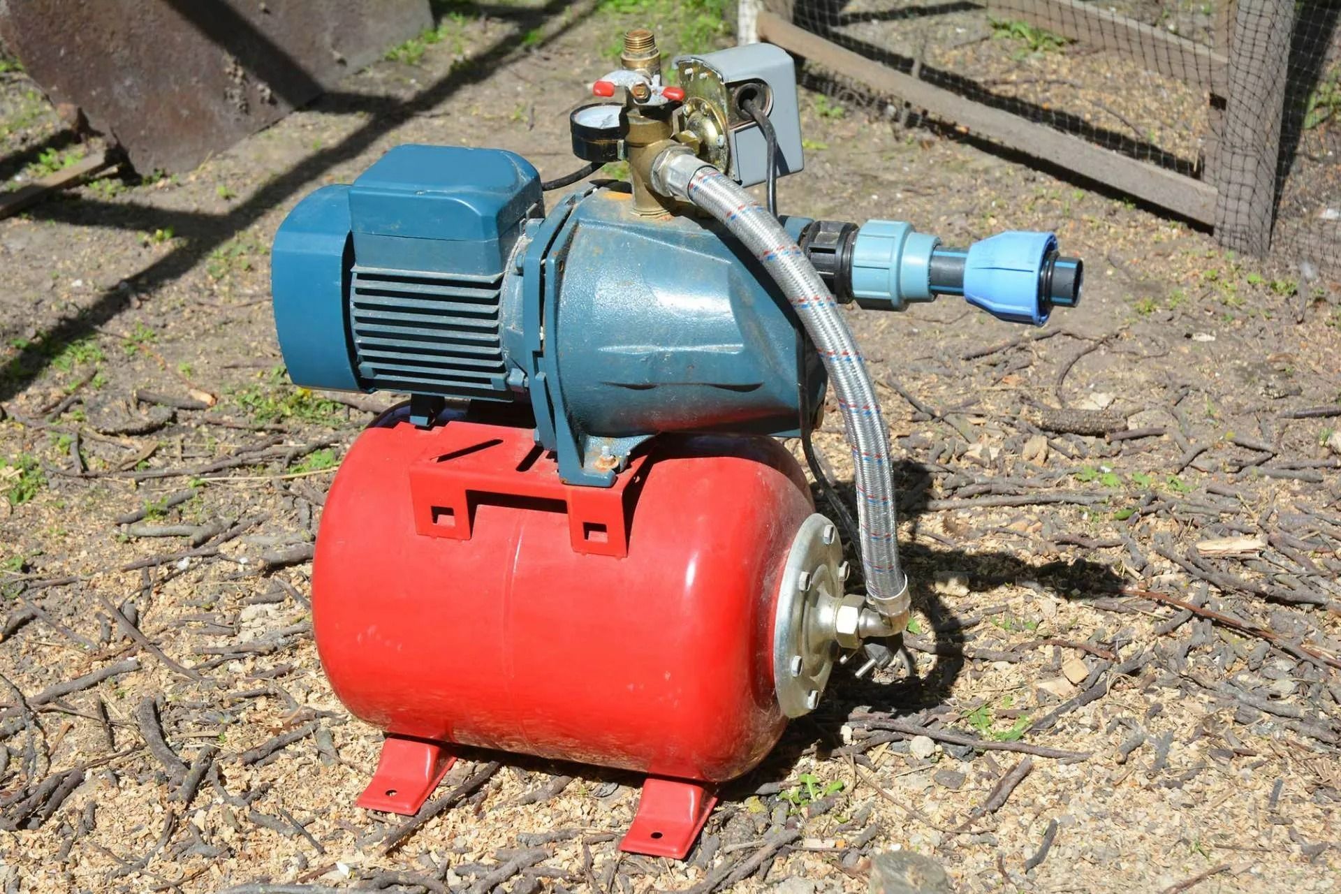 A water pump is sitting on the ground next to a red tank.