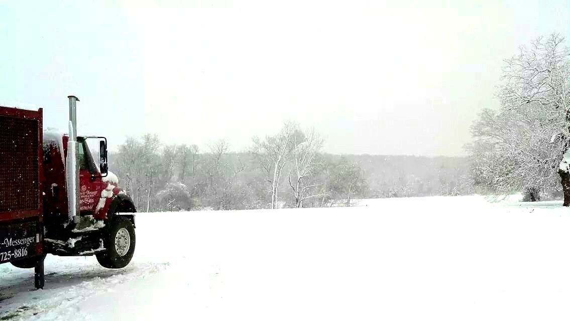 A red semi truck is driving through a snowy field.
