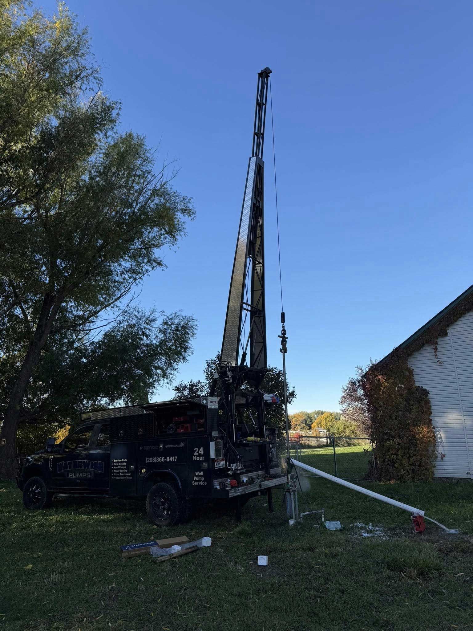 Drilling rig on a trailer in a grassy yard, beside a house with a clear blue sky background.