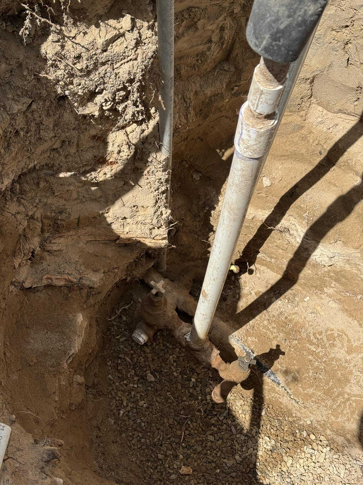 Pipes in a dirt trench, possibly for irrigation or plumbing; sunlight.