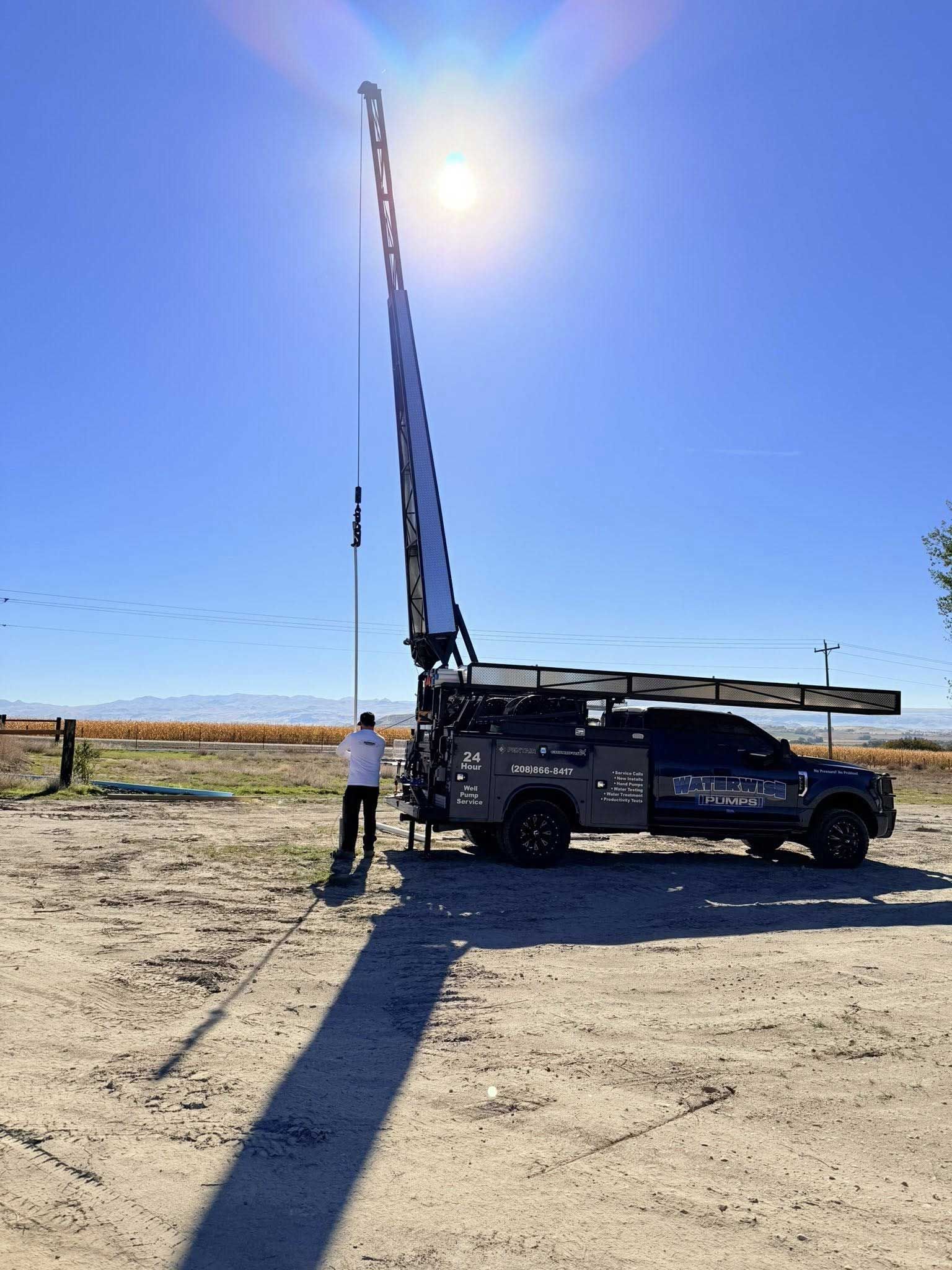 Truck with crane extended high in the air under a bright sun, person standing nearby.