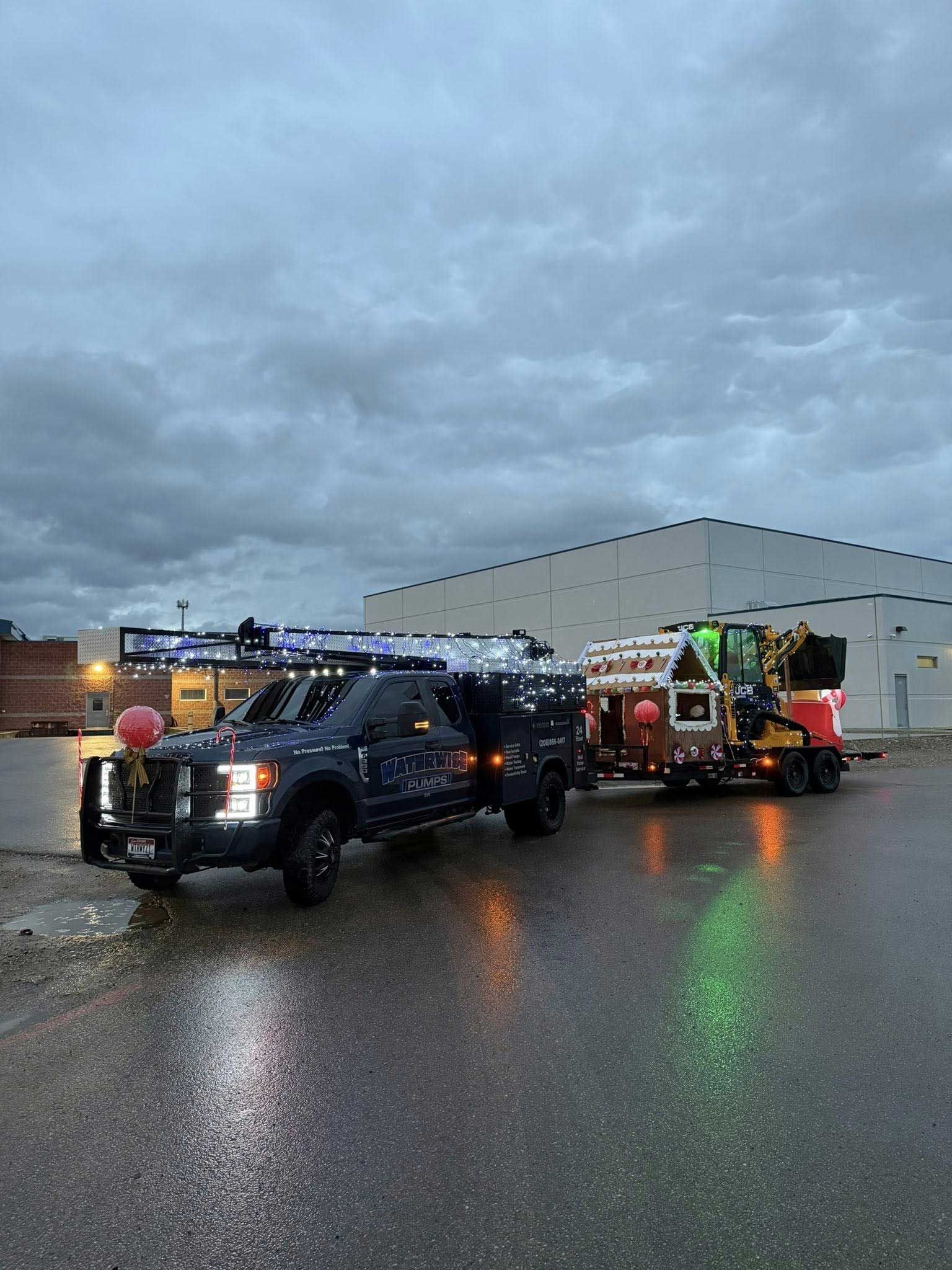 Dark truck towing a trailer, both decorated with lights, under a cloudy sky.