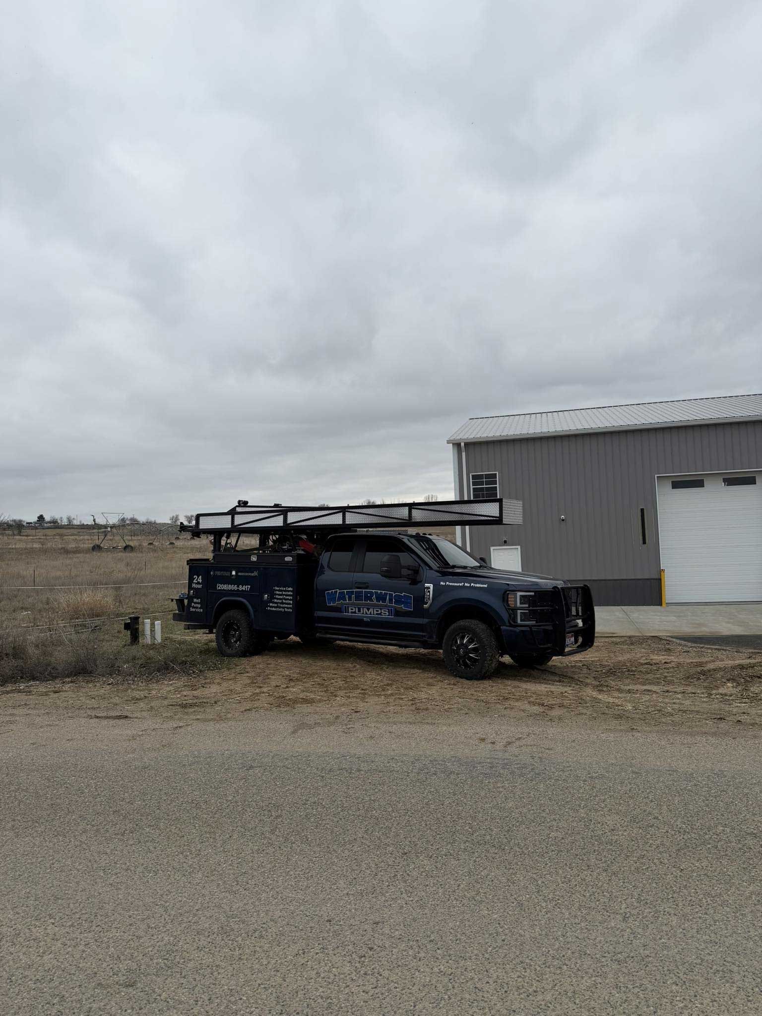 Dark blue work truck with equipment on the roof parked by a building on a cloudy day.