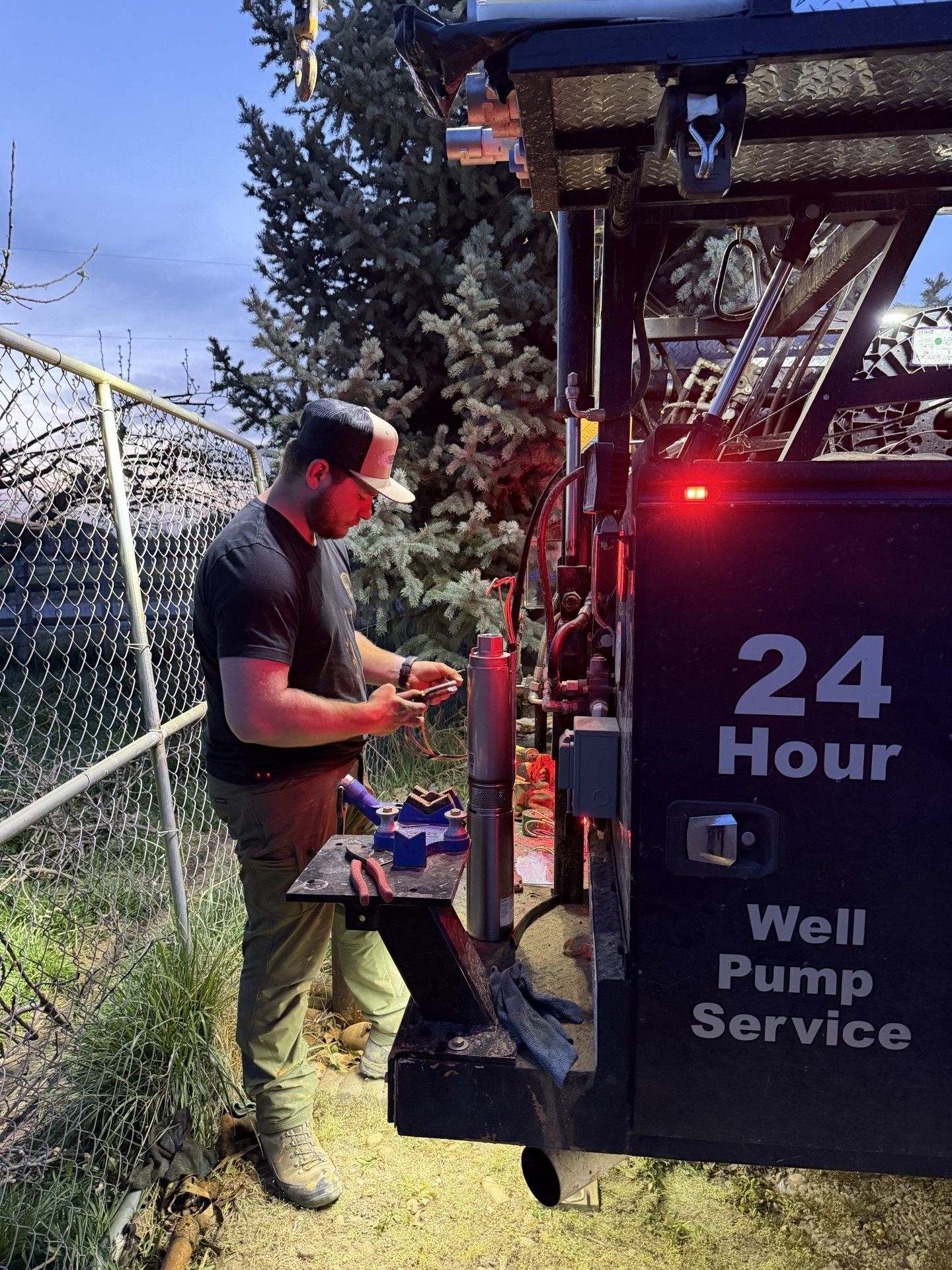 A service technician works on equipment at the back of a black service truck labeled 