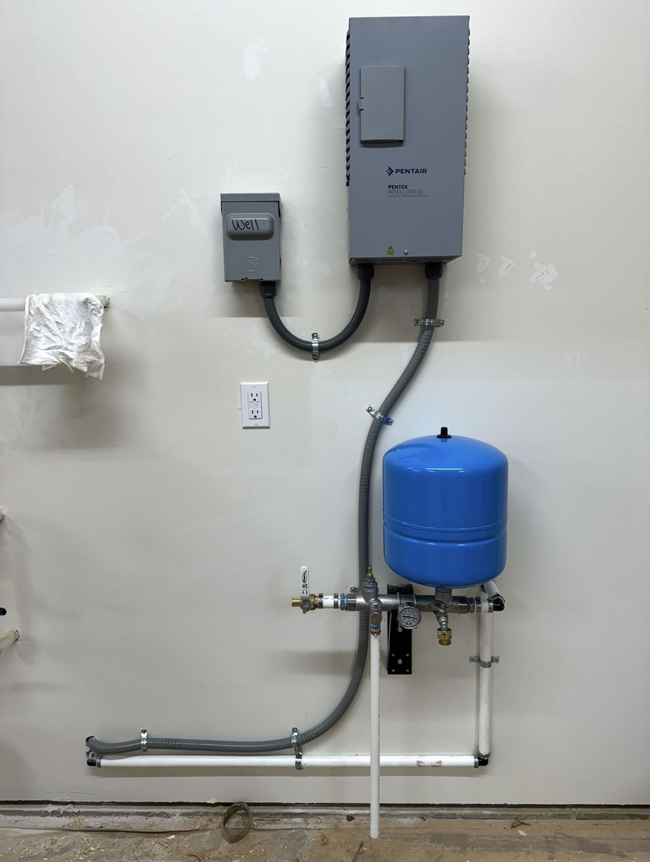 Electrical control boxes connected to a water pressure tank and pipes mounted on a white wall.