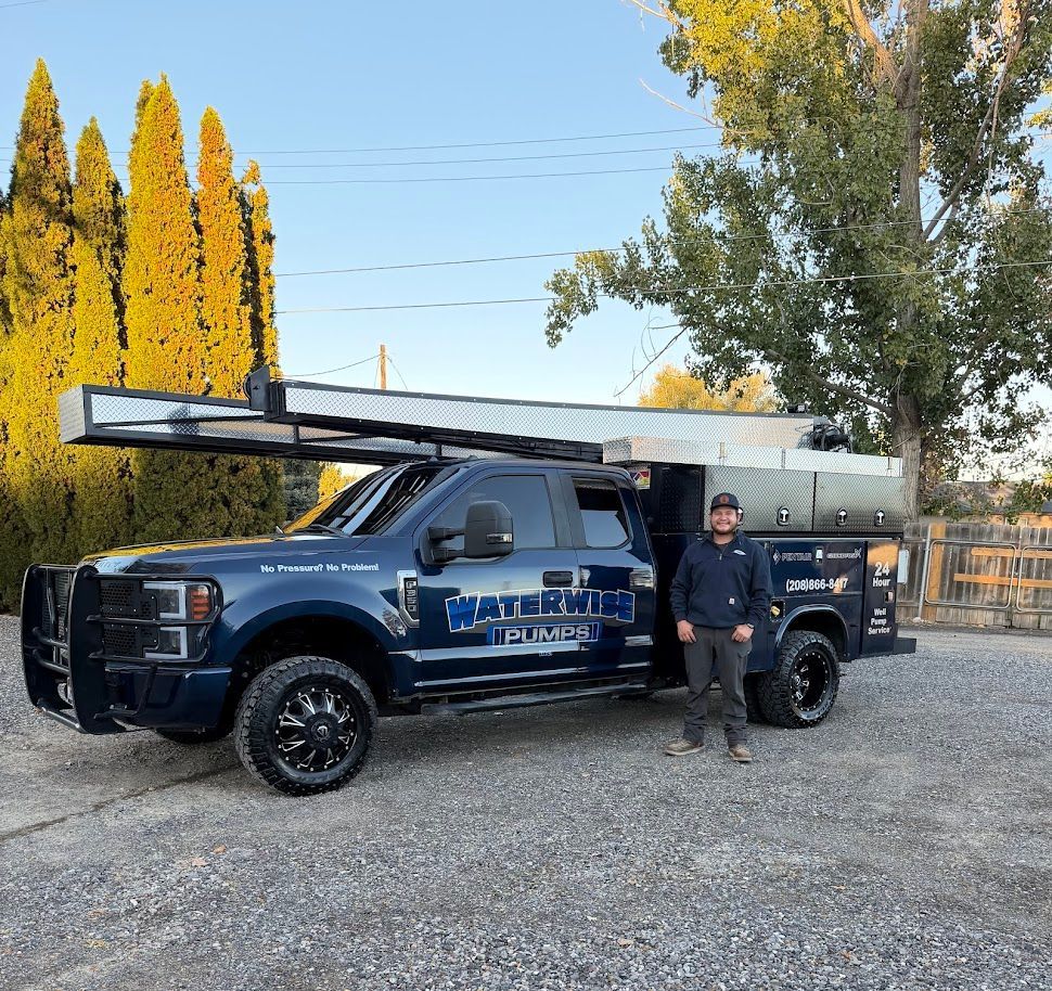 A person stands next to a dark blue WaterKing Pumps utility truck with a ladder rack, parked on a gravel lot.