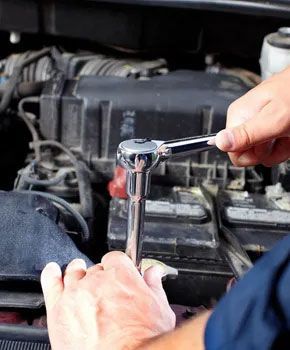 Hands using a chrome ratchet wrench to tighten a bolt on a car engine.
