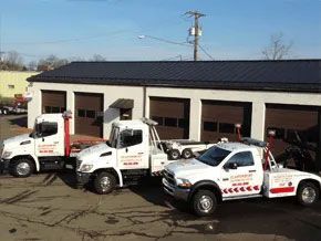 Three white tow trucks parked in front of a building with four brown garage doors under a clear blue sky.