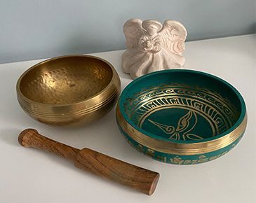 A brass bowl, a green bowl, and a wooden mortar and pestle are on a table.