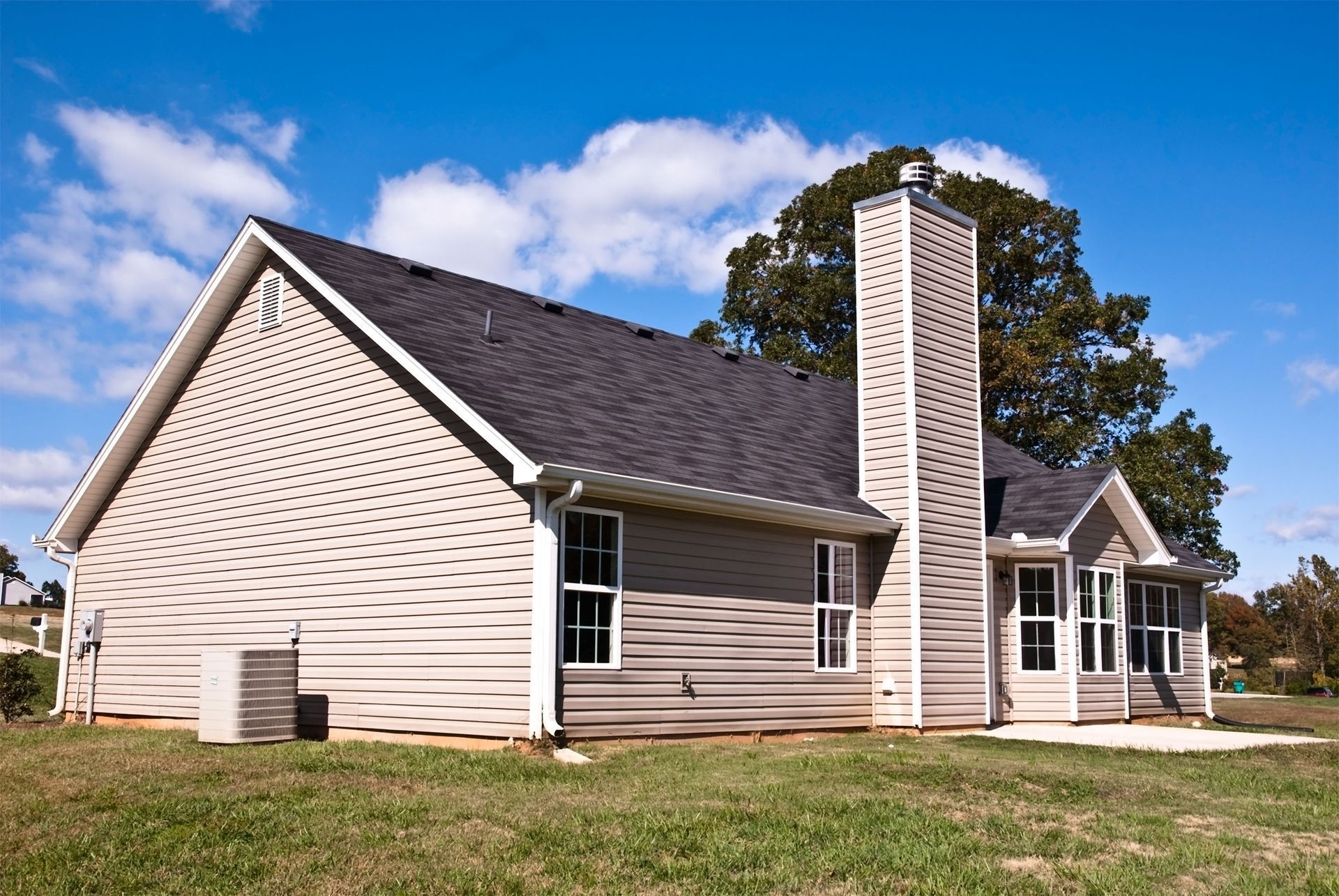 House with light-colored siding, dark roof, tall chimney, and white-framed windows against a blue sky.