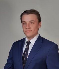 A man in a suit and tie is standing in front of a white background.