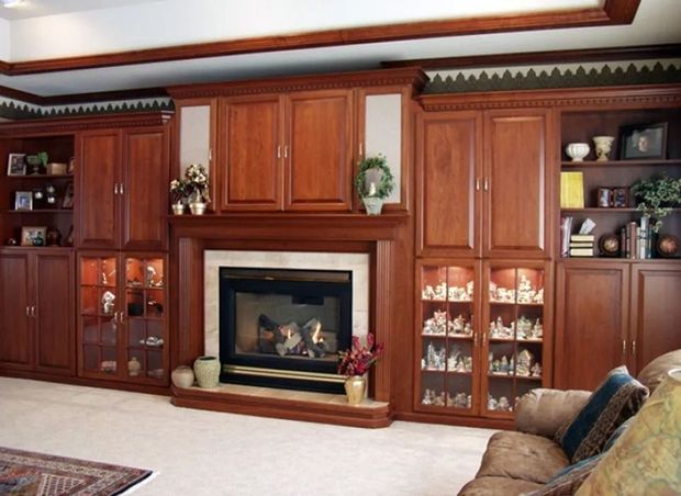 Built-in wooden cabinetry surrounds a fireplace. Display cabinets hold figurines; a brown sofa sits nearby.