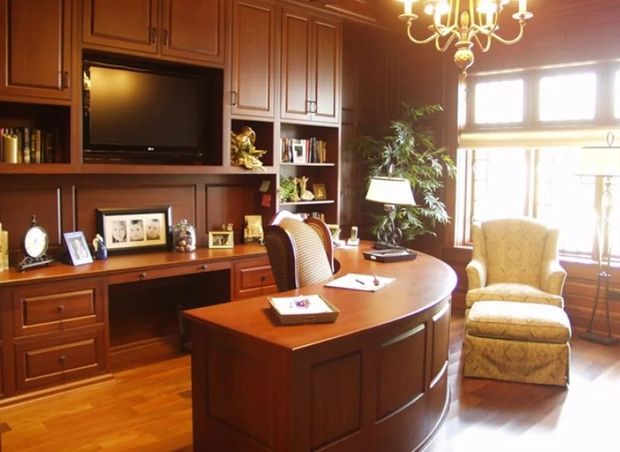 Elegant wooden home office with built-in desk, cabinets, TV, and decorative items.