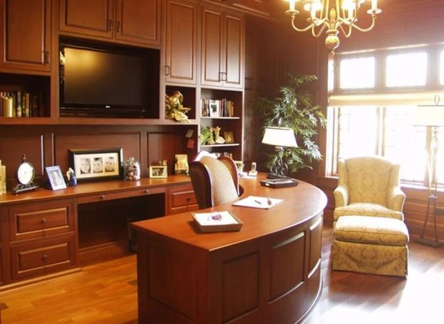 Elegant wooden home office with built-in desk, cabinets, TV, and decorative items.