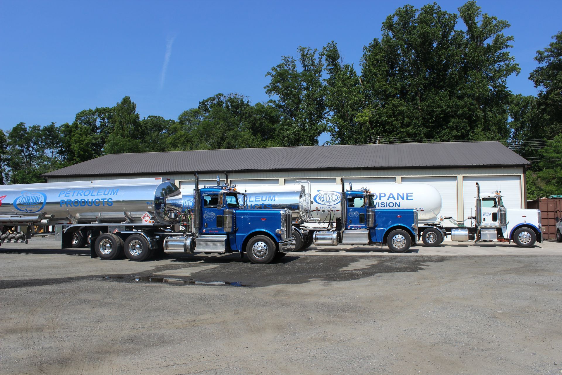 Two tanker trucks parked in front of a white industrial building under a blue sky