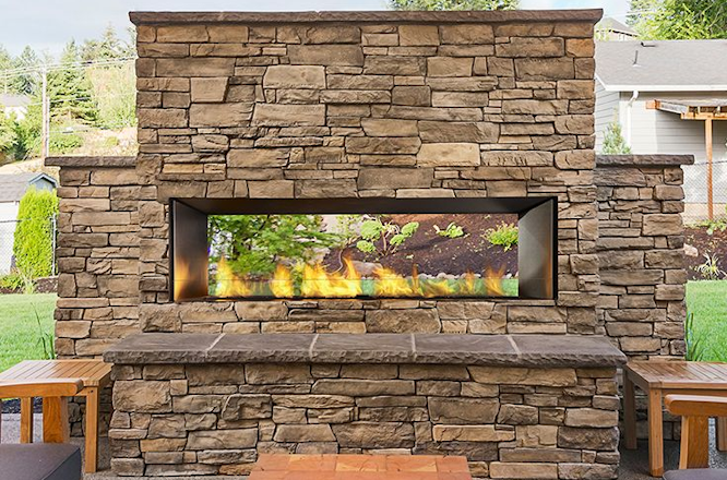 Stone outdoor fireplace with a long horizontal firebox and flames burning in a patio setting