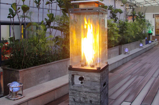 Outdoor fire feature with bright flames in a planter-lined walkway at dusk