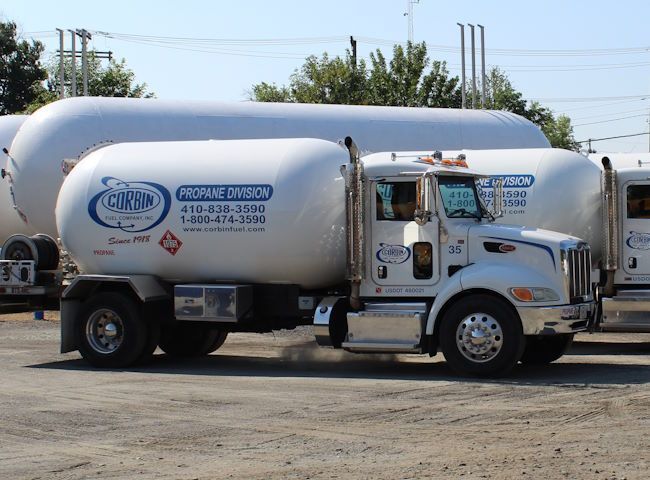 White propane delivery truck with tanker parked in a lot under a blue sky