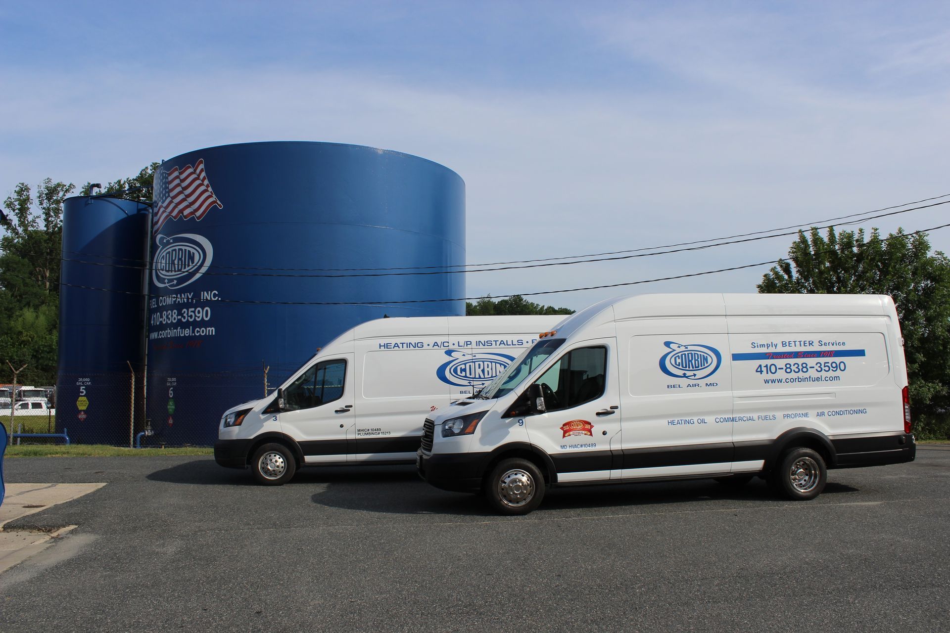 Two white service vans parked beside a large blue industrial tank under a clear sky.
