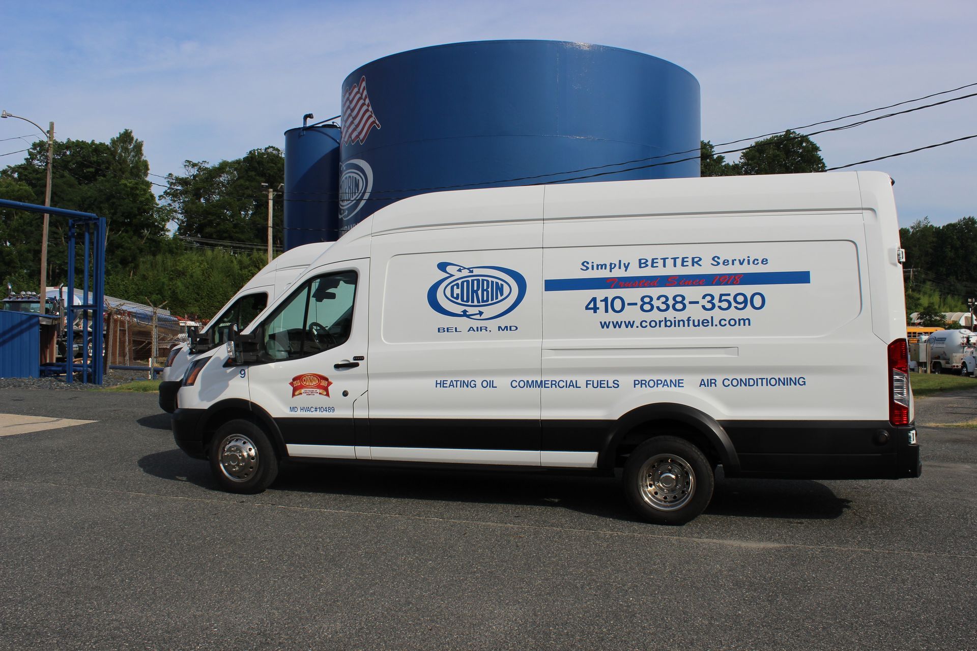 White service van parked beside a blue water tank in an industrial lot, with company branding on the side.