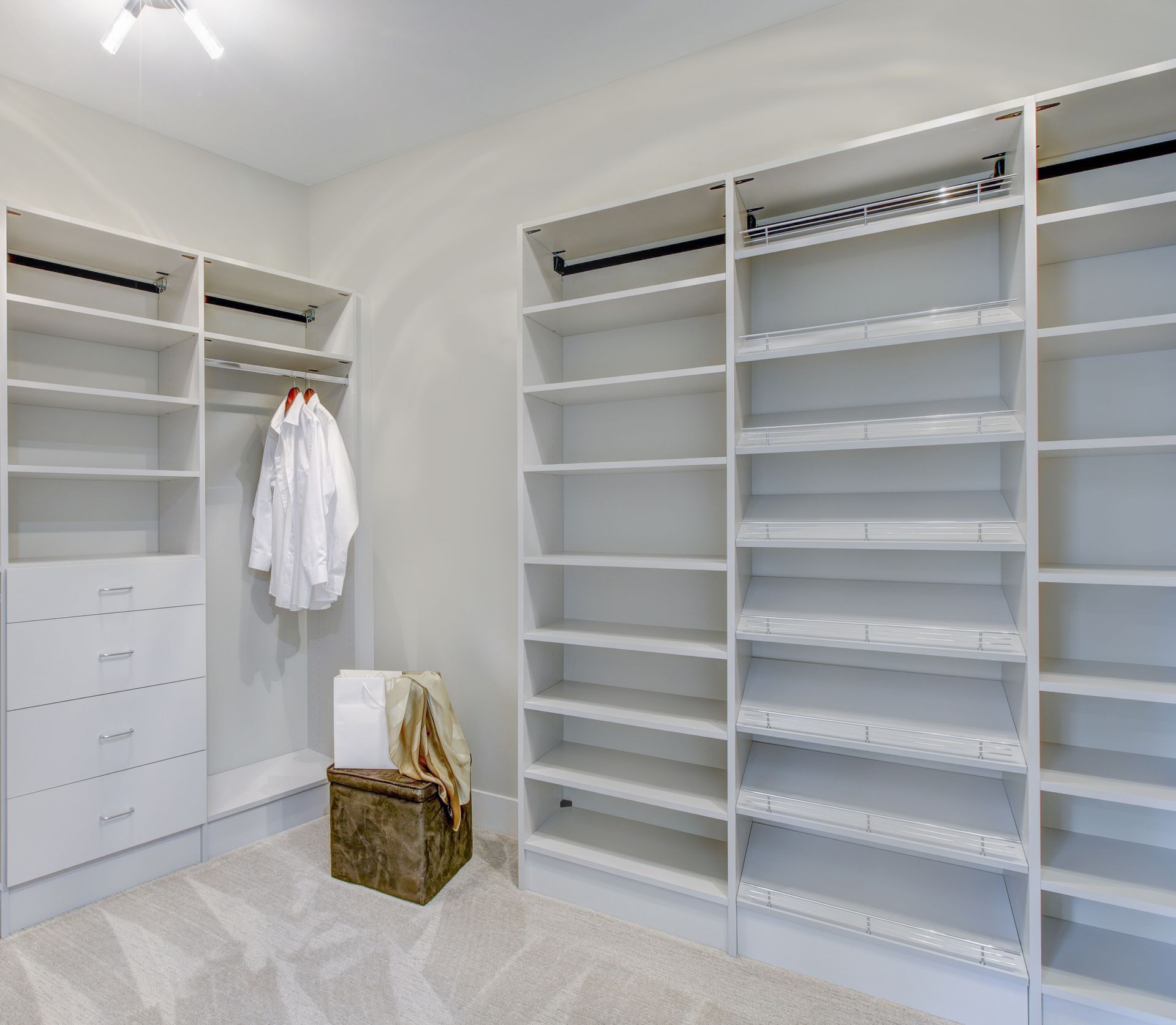 White built-in closet with shelves, drawers, and hanging rod. A shirt hangs on the rod, and a trunk sits on the floor.