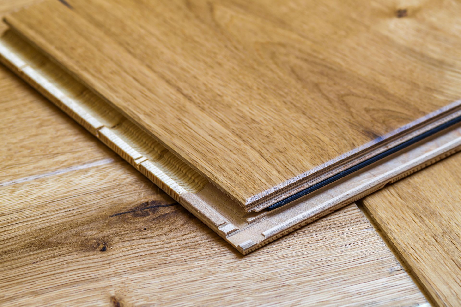 Close-up of interlocking wooden floor planks. Beige and brown tones. Tongue-and-groove system visible.