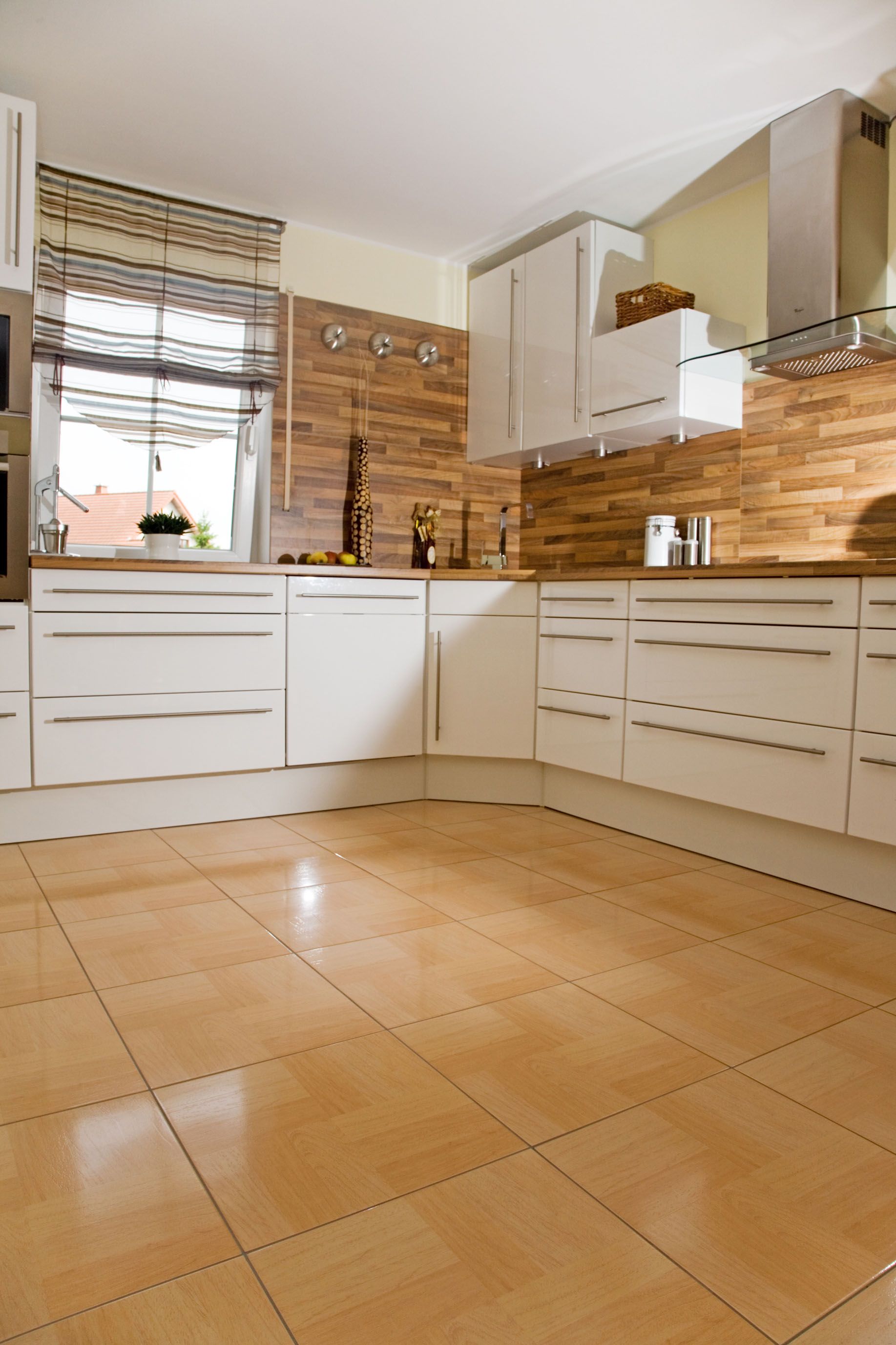 Modern kitchen with white cabinets, wood backsplash, and light-colored tiled floor.