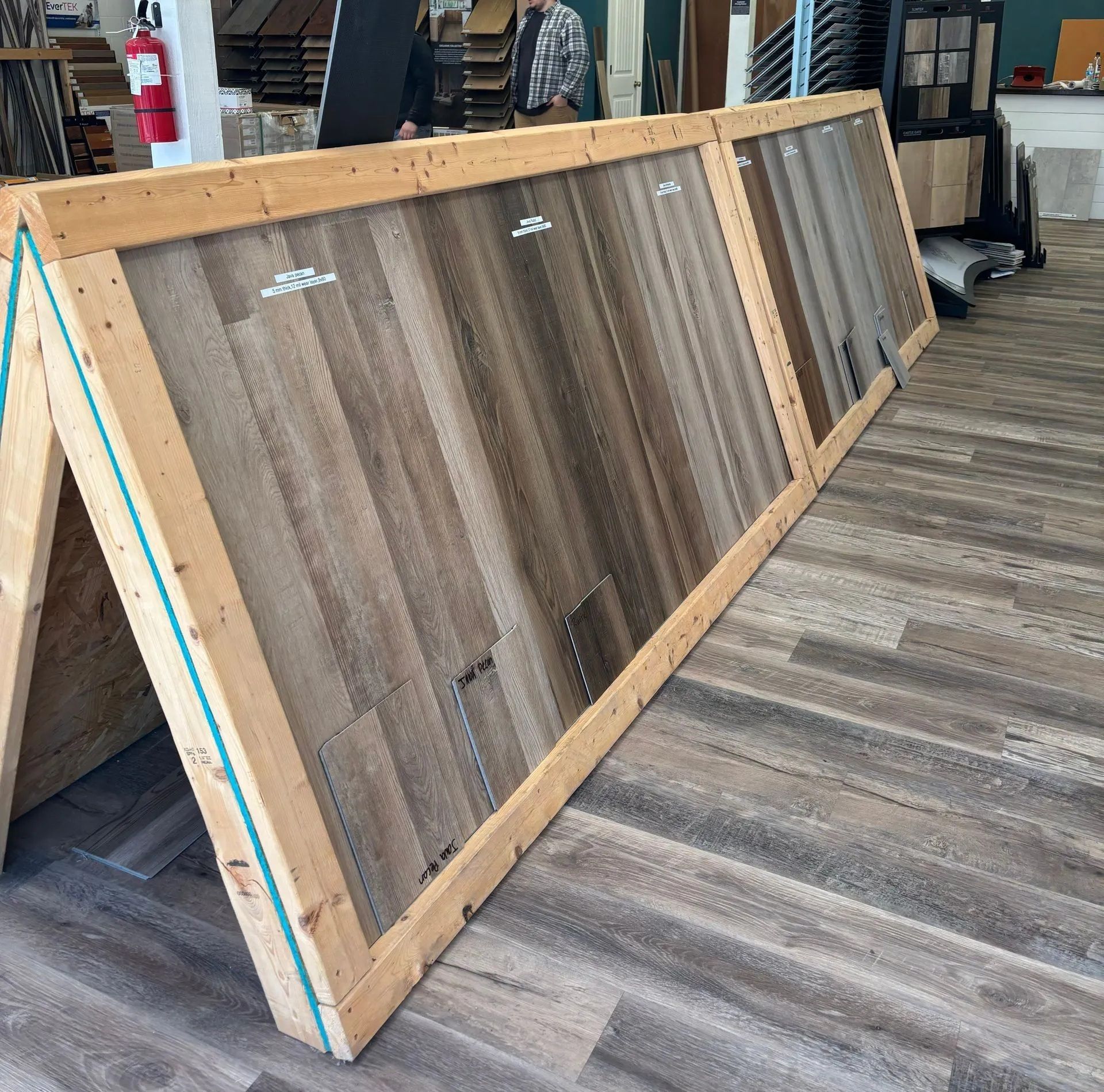 Three wooden display boards of flooring samples, leaning against each other. Interior shot of a showroom.