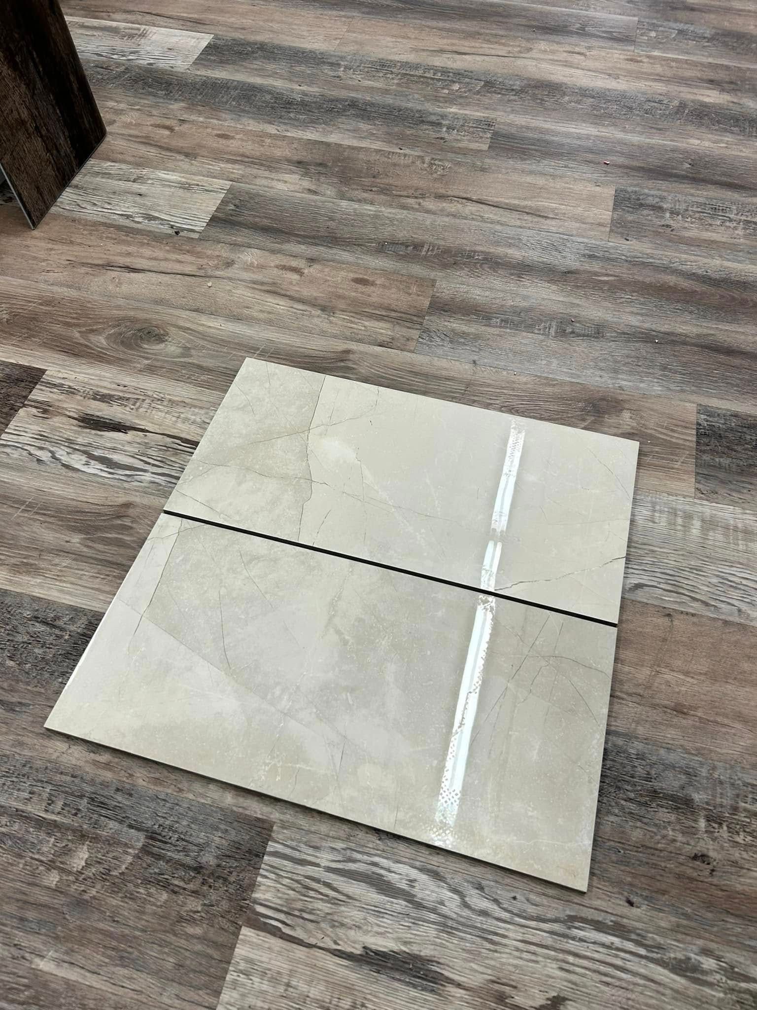 Tile sample on wood-look flooring. Light gray tile with a white stripe and a black line on it.